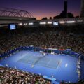 Twilight sets over a bustling Australian Open tennis match, showcasing players in action with a packed stadium audience, ideal for exploring sports travel packages.