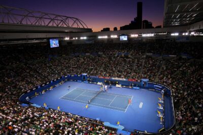 Twilight sets over a bustling Australian Open tennis match, showcasing players in action with a packed stadium audience, ideal for exploring sports travel packages.