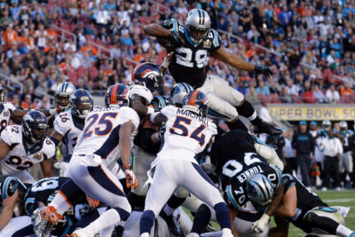 Intense moment at a Super Bowl game showing a player leaping over others during a pivotal play, capturing the thrilling atmosphere of this must-see sporting event.