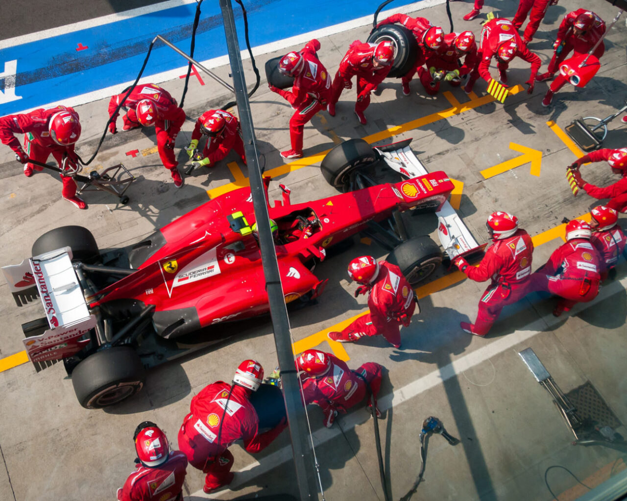 Pit crew in red uniforms perform a tire change and maintenance on a red race car during the Italian Grand Prix, showcasing speed and teamwork in motorsports.