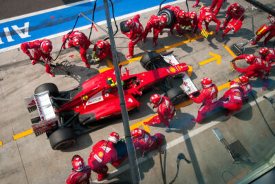 Pit crew in red uniforms perform a tire change and maintenance on a red race car during the Italian Grand Prix, showcasing speed and teamwork in motorsports.