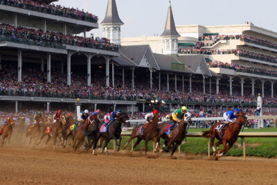 Horses race on a dirt track in front of a packed grandstand at the Kentucky Derby, showcasing the event's excitement and tradition.