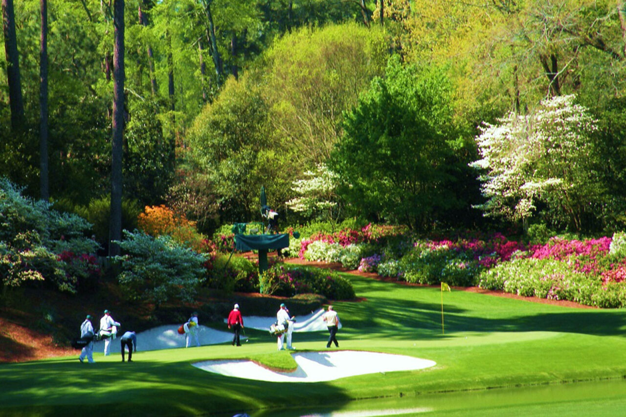 Golfers and caddies on a vibrant, flower-lined course at the Masters, reflecting luxury sports travel and etiquette in Augusta.