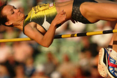 An athlete in a yellow and green uniform performs a high jump at a Summer Games event, showcasing determination and skill.