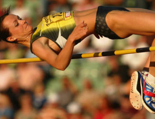 An athlete in a yellow and green uniform performs a high jump at a Summer Games event, showcasing determination and skill.