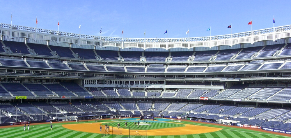 Empty baseball stadium with a detailed view of the field and stands under a clear blue sky, showcasing one of the greatest sights in New York for sports fans.