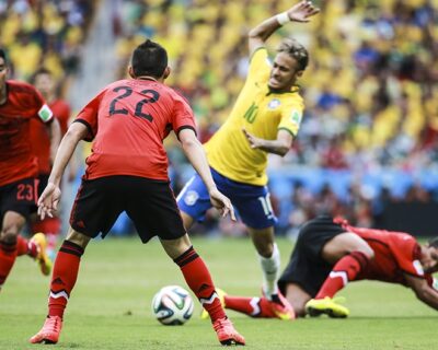 Players from Brazil and Mexico compete during a soccer match, capturing dynamic action as one player maneuvers around fallen opponents.