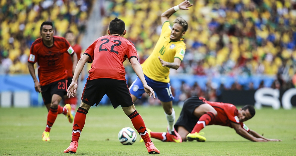 Players from Brazil and Mexico compete during a soccer match, capturing dynamic action as one player maneuvers around fallen opponents.
