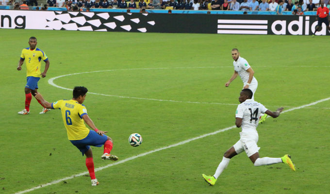A soccer player in a yellow and blue uniform kicks the ball towards an opponent in white during a match, providing an action-packed moment for World Cup Custom Getaways.
