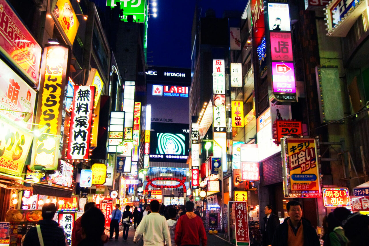 Vibrant night view of a busy street in Shinjuku, Tokyo, filled with colorful neon signs and bustling with pedestrians, showcasing the city's lively urban atmosphere.