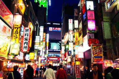 Vibrant night view of a busy street in Shinjuku, Tokyo, filled with colorful neon signs and bustling with pedestrians, showcasing the city's lively urban atmosphere.