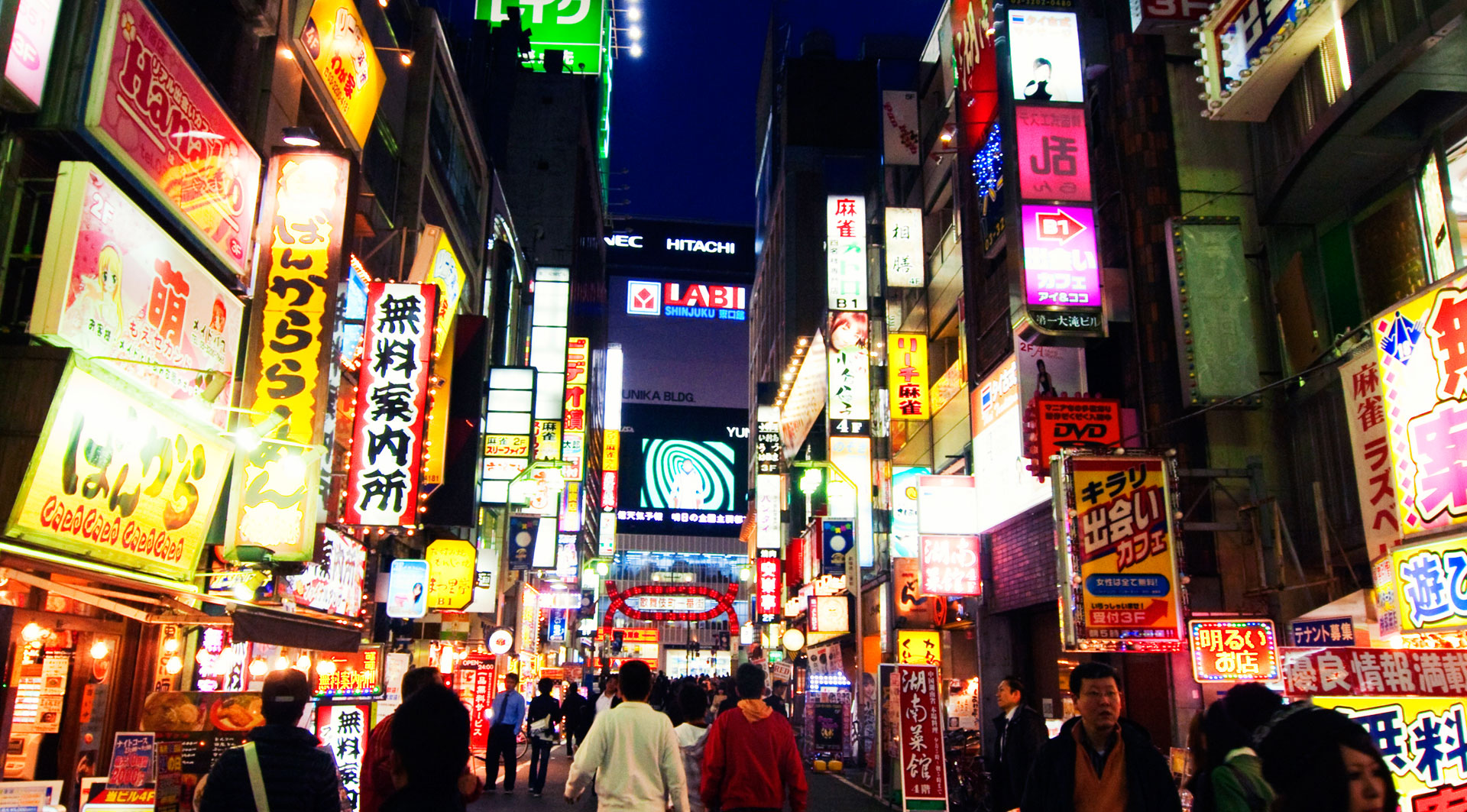 Vibrant night view of a busy street in Shinjuku, Tokyo, filled with colorful neon signs and bustling with pedestrians, showcasing the city's lively urban atmosphere.