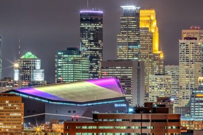 Nighttime view of downtown Minneapolis skyline with illuminated buildings and a prominent sports stadium, highlighting top Super Bowl activities.