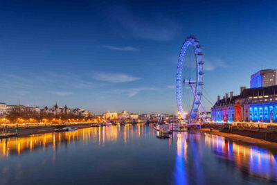 Twilight view of the illuminated London Eye beside the River Thames, reflecting cultural and entertainment aspects during the Wimbledon season.