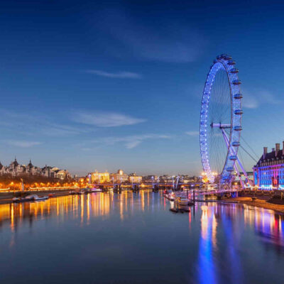 Twilight view of the illuminated London Eye beside the River Thames, reflecting cultural and entertainment aspects during the Wimbledon season.