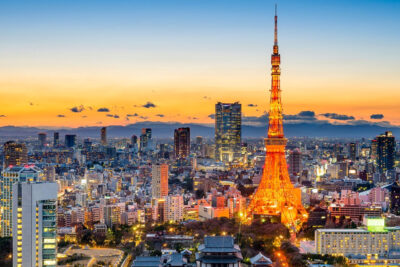 Sunset view of Tokyo skyline featuring the illuminated Tokyo Tower, framed by modern buildings and distant mountains, ideal for exploring during the Summer Games.