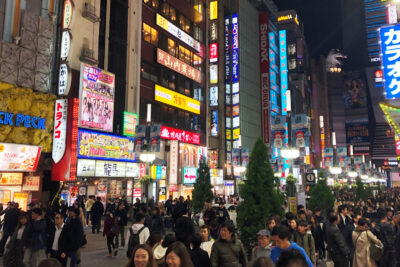 Crowded Tokyo street at night, illuminated by numerous colorful signs and billboards, with many people walking, best for visiting during the Summer Games.
