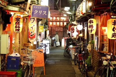 Colorful nighttime view of a vibrant alley in Tokyo, lined with traditional lanterns and quaint eateries, showcasing a typical street scene in one of Tokyo's bustling neighborhoods.