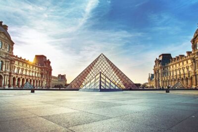 Sunset view at the Louvre Museum in Paris featuring the iconic glass pyramid and historical architecture.
