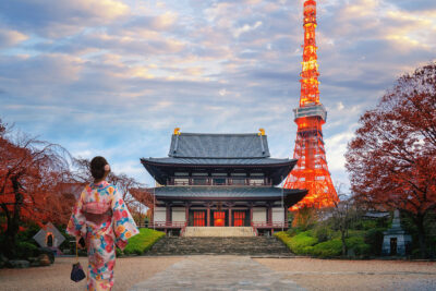 Woman in a colorful kimono admires the illuminated Tokyo Tower and a traditional Japanese temple at sunset, highlighting cultural landmarks in Tokyo.
