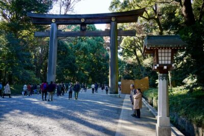 Visitors walk under a traditional torii gate at Yoyogi Koen Park in Shibuya, Tokyo, highlighting a serene setting ideal for exploring during the Summer Games.