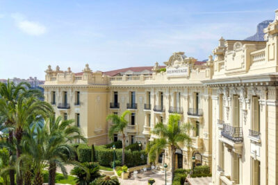 Elegant view of Hotel Hermitage, a prime accommodation recommendation for visitors attending the Monaco Grand Prix, showcasing its classic architecture and lush, palm-fringed gardens.