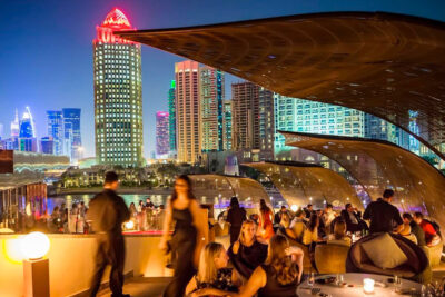 People enjoy an evening at an upscale outdoor dining area with a view of Doha's illuminated skyline.