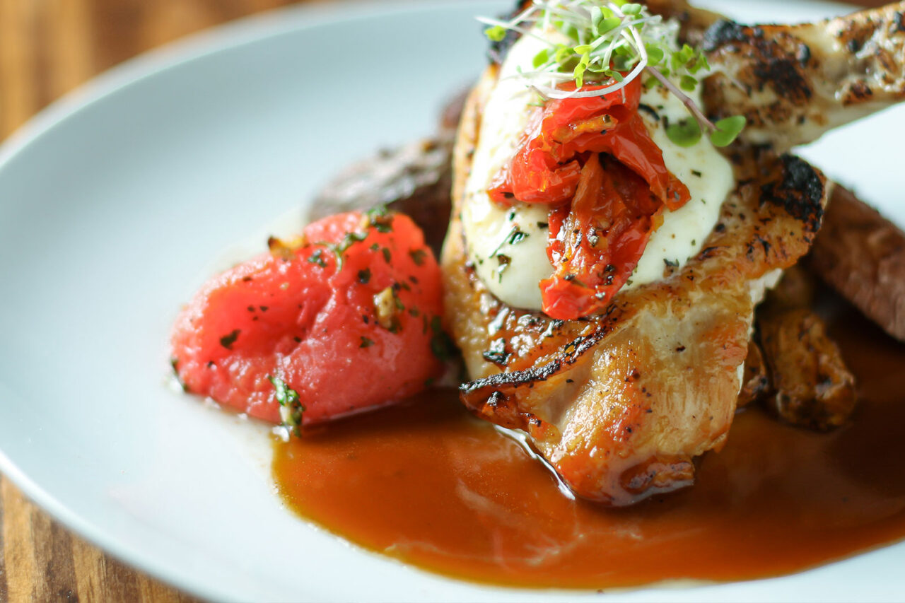 Grilled chicken topped with melted cheese and sun-dried tomatoes, served with herbed potatoes and watermelon, representing a culinary feature in Augusta during the Masters.