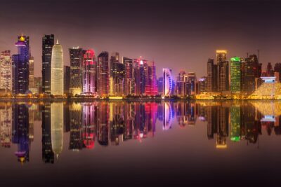 A vibrant nighttime view of Doha's skyline reflecting in the water, showcasing a range of illuminated modern buildings and towers.