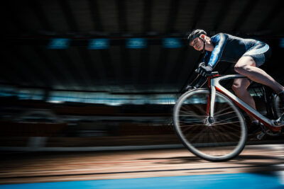 A cyclist in a blue and white suit speeds around a velodrome, captured in motion blur, highlighting the excitement of sports travel experiences.