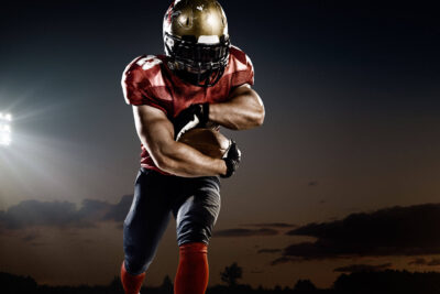 Football player in red uniform clutching a ball, showcasing a Super Bowl handoff play against a dusk sky backdrop.
