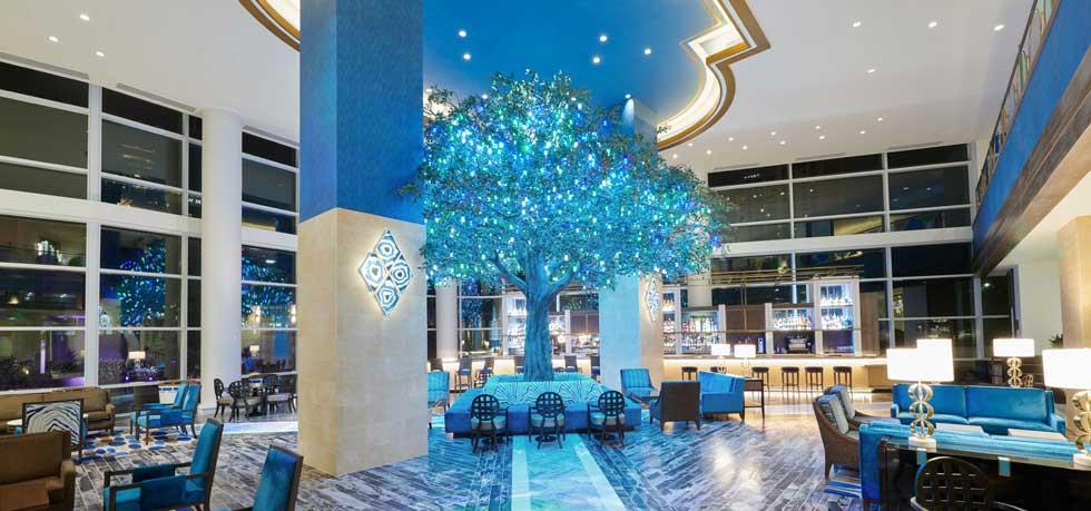 Luxurious lobby at Fairmont Austin, featuring a striking illuminated blue tree centerpiece, stylish furniture, and modern decor, perfect for guests attending the US Grand Prix in Austin, Texas.