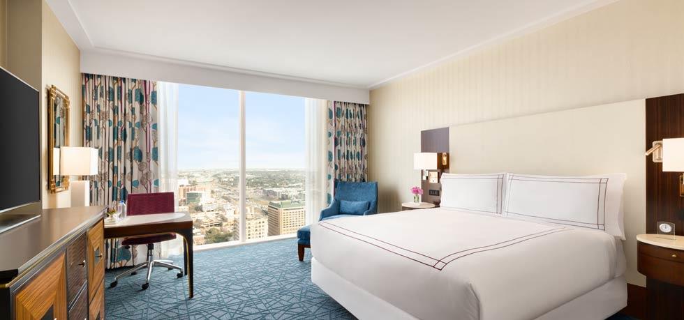 Luxurious hotel room with a large bed, contemporary decor, and panoramic city views from floor-to-ceiling windows, available for the US Grand Prix in Austin, Texas.