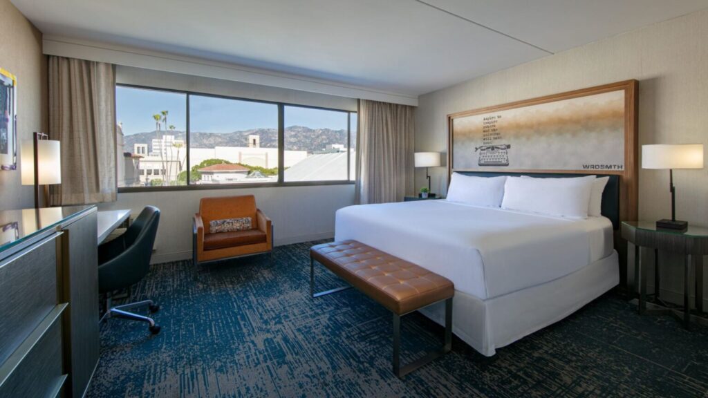 A luxurious hotel room at Hotel Dena in Pasadena, featuring a modern design with a large window offering views of the surrounding buildings, ideal for visitors to the Rose Bowl.