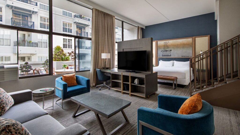 Interior view of a luxurious hotel room at Hotel Dena in Pasadena, California, featuring modern furnishings, large windows with city view, and a loft-style bedroom ideal for Rose Bowl visitors.