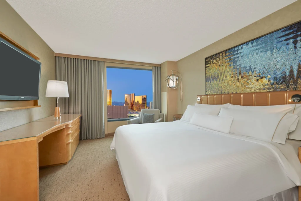 Interior of a hotel room at Westin Las Vegas Hotel & Spa, showcasing a large bed, a desk, and a view of the sunset over Las Vegas, fitting for the Las Vegas Grand Prix Hotels.