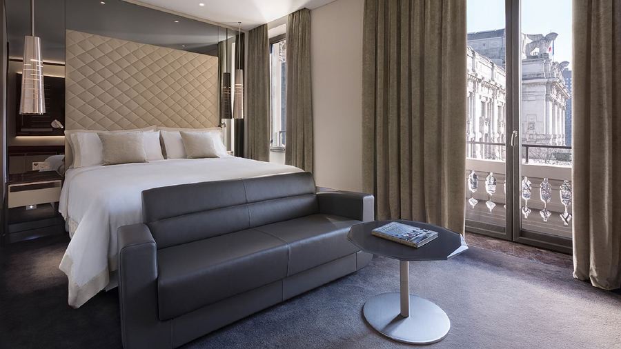 Luxury hotel room in Milan featuring a large bed, modern sofa, and a view of Piazza Duca D’Aosta, ideal for Italian Grand Prix attendees seeking accommodations.