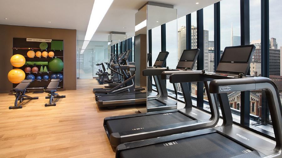 Modern gym with treadmills and exercise equipment at Excelsior Hotel Gallia, showing views of Milan's cityscape, ideal for Italian Grand Prix accommodations.