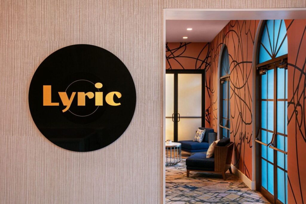Interior of a stylish hotel, showcasing a black Lyric logo on a textured wall and a vibrant, decorated hallway reflecting luxury accommodation options for the Rose Bowl in Pasadena, California.