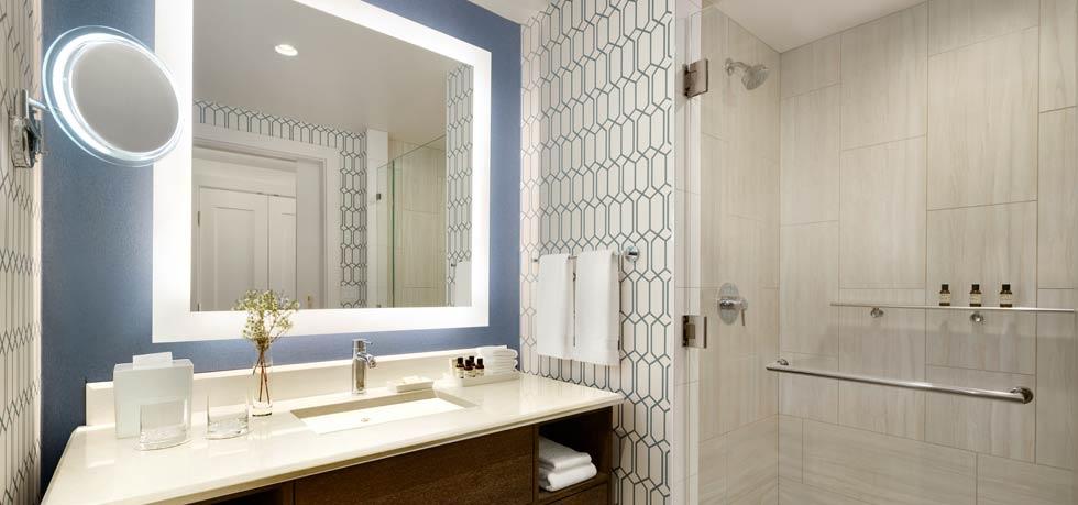 Modern bathroom interior featuring a large mirror, a white countertop with sink, and a tiled shower at the Fairmont Austin, Texas, near the US Grand Prix.