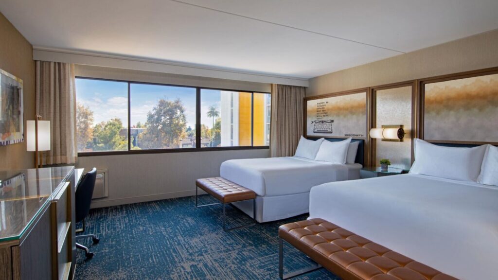 Luxury hotel room at Hotel Dena, a Marriott Tribute Portfolio Hotel, featuring two beds, a work desk, and large windows with a view, located at 303 Cordova Street in Pasadena, California. Ideal for Rose Bowl visitors.