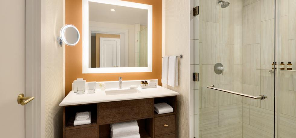 Well-lit modern bathroom featuring a spacious vanity with mirror and an adjacent glass-door shower, ideal for guests at US Grand Prix hotels in Austin, Texas.