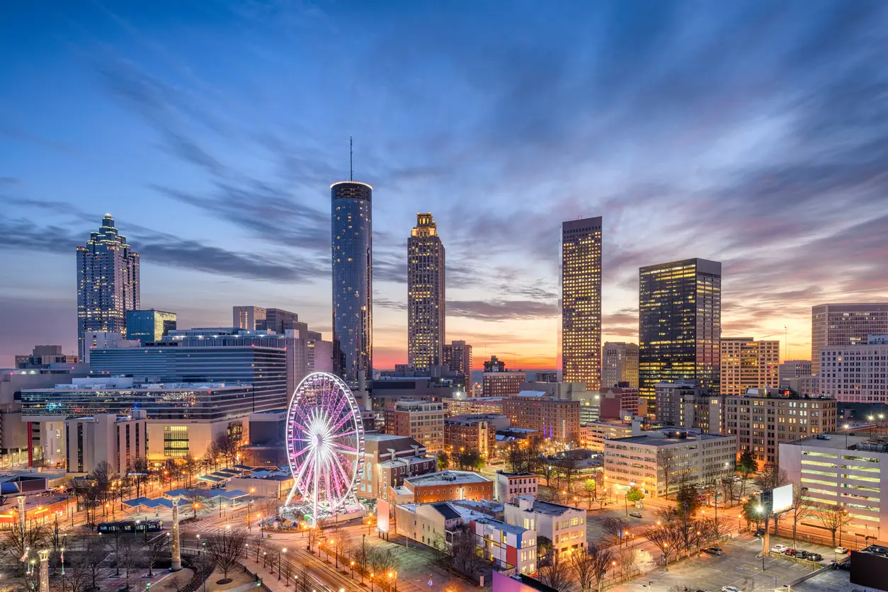 Sunset view of Atlanta's skyline featuring illuminated skyscrapers and a Ferris wheel, highlighting the city as a World Cup host with the Mercedes-Benz Stadium.