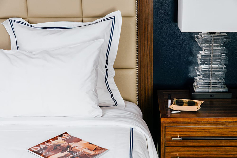 Elegant hotel room setup at The Adolphus in Dallas, featuring a plush bed with a magazine and glasses on the side table, ideal for World Cup travelers seeking luxurious accommodations.