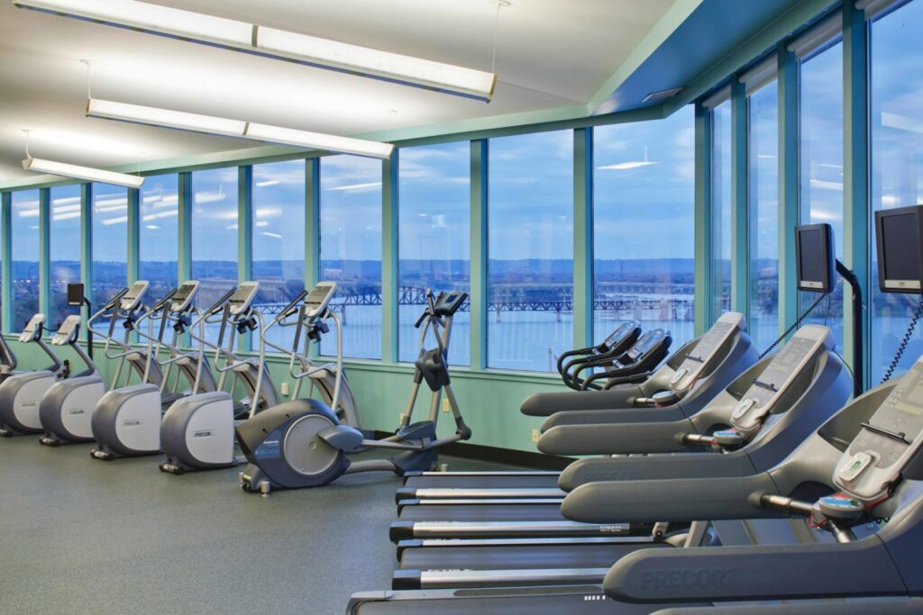 Gym with treadmills and elliptical machines facing large windows overlooking a river, located at the Galt House Hotel near Churchill Downs, ideal for visitors of the Kentucky Derby.