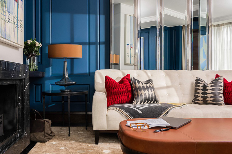 Luxurious room in Corinthia Hotel London featuring a white sofa with stylish cushions, a marble fireplace, and blue walls, ideal for Wimbledon Championships guests seeking accommodations.