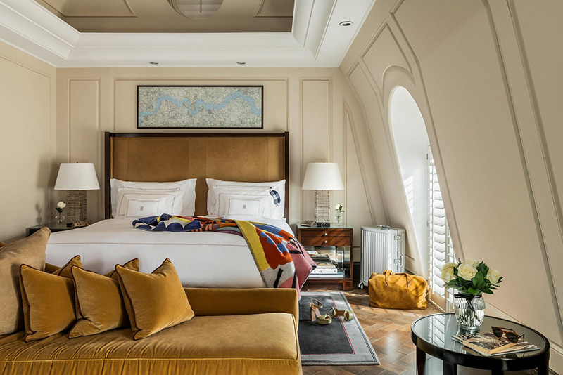 Luxurious hotel room at the Corinthia Hotel London, featuring an elegant bed with plush pillows, arching windows, and refined decor, ideal for guests attending the Wimbledon Championships.