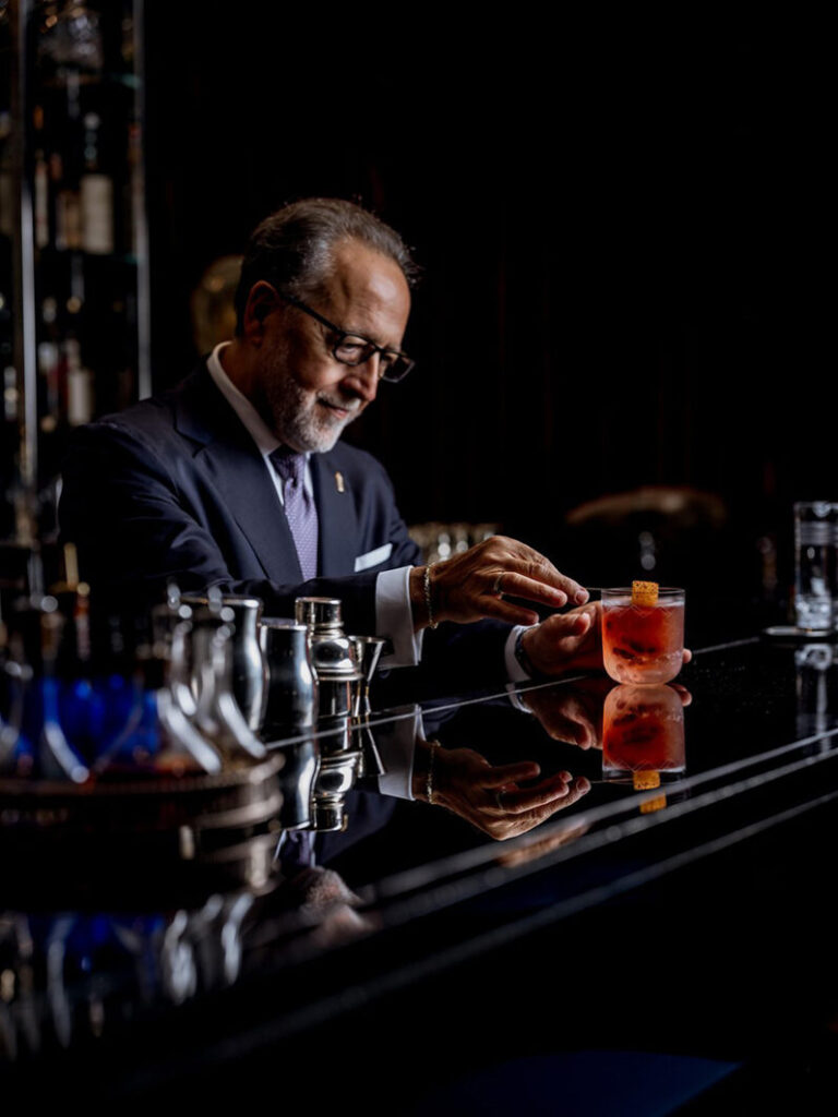 A skilled bartender at the Corinthia Hotel London, dressed formally, carefully prepares a cocktail, ideal for guests seeking luxury accommodations near the Wimbledon Championships in London.