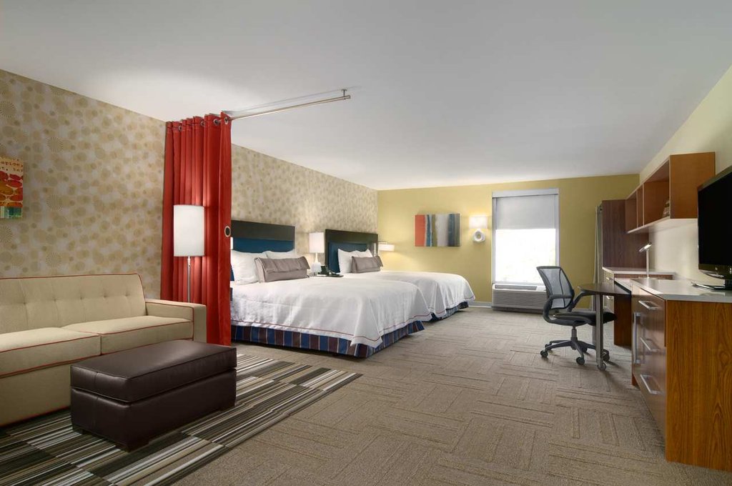 Bright and modern suite at Hilton Home2 Suites in Augusta, Georgia, featuring two queen beds, a seating area, desk space, and kitchenette, ideal for guests visiting for the Masters golf tournament.