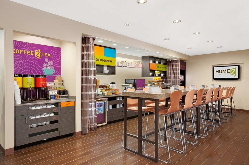 Spacious breakfast area at Home2 Suites by Hilton in Augusta, featuring a self-service coffee station, modern seating, and vibrant decor, ideal for visitors seeking accommodations near Augusta's golf events.
